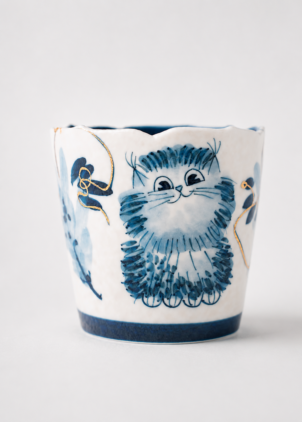 A white ceramic planter with a hand-painted blue and gold illustration of a fluffy cat, shown on a light gray background.