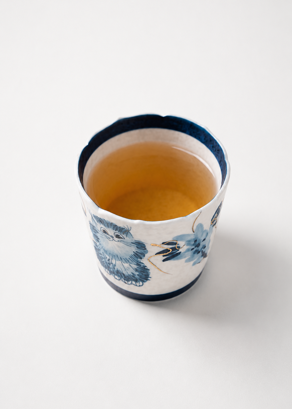 A small white ceramic cup with blue floral patterns and a dark blue rim, filled with amber tea, photographed on a clean white background.