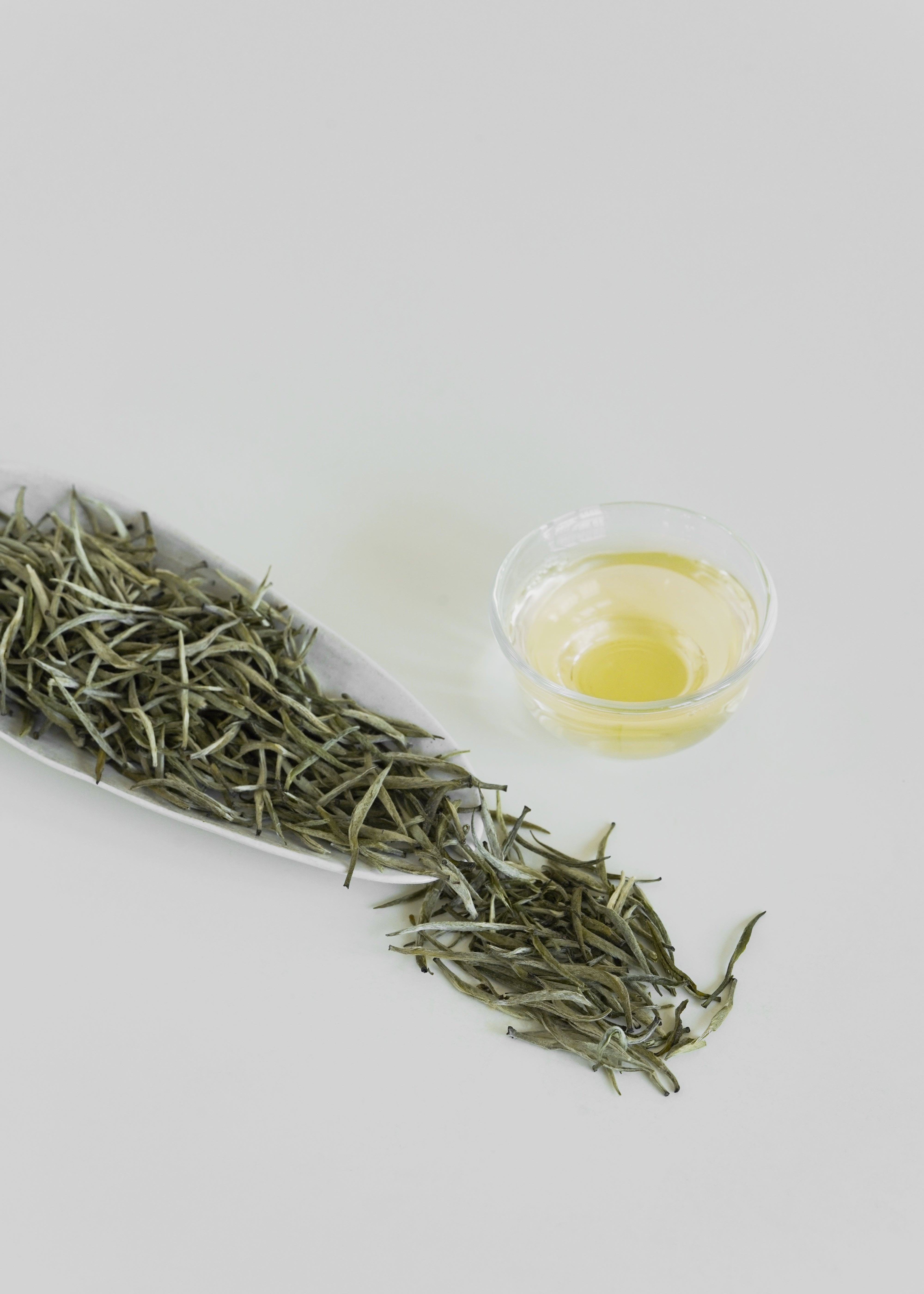 Dry green tea leaves and a small glass of tea on a light gray background. Orchid yellow tea