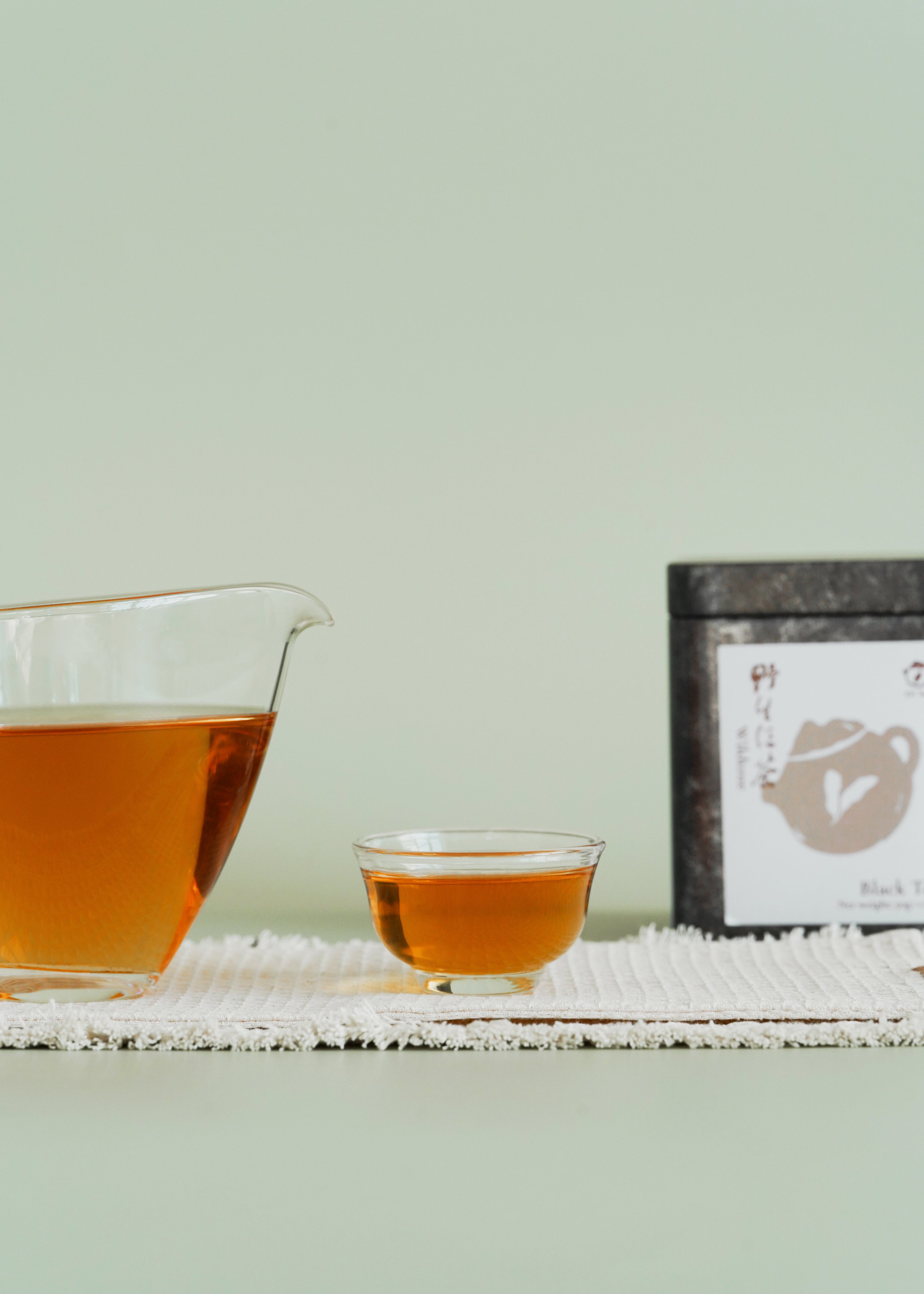 Tea cup and teapot with a tea package on a light green background. Wild tree black tea
