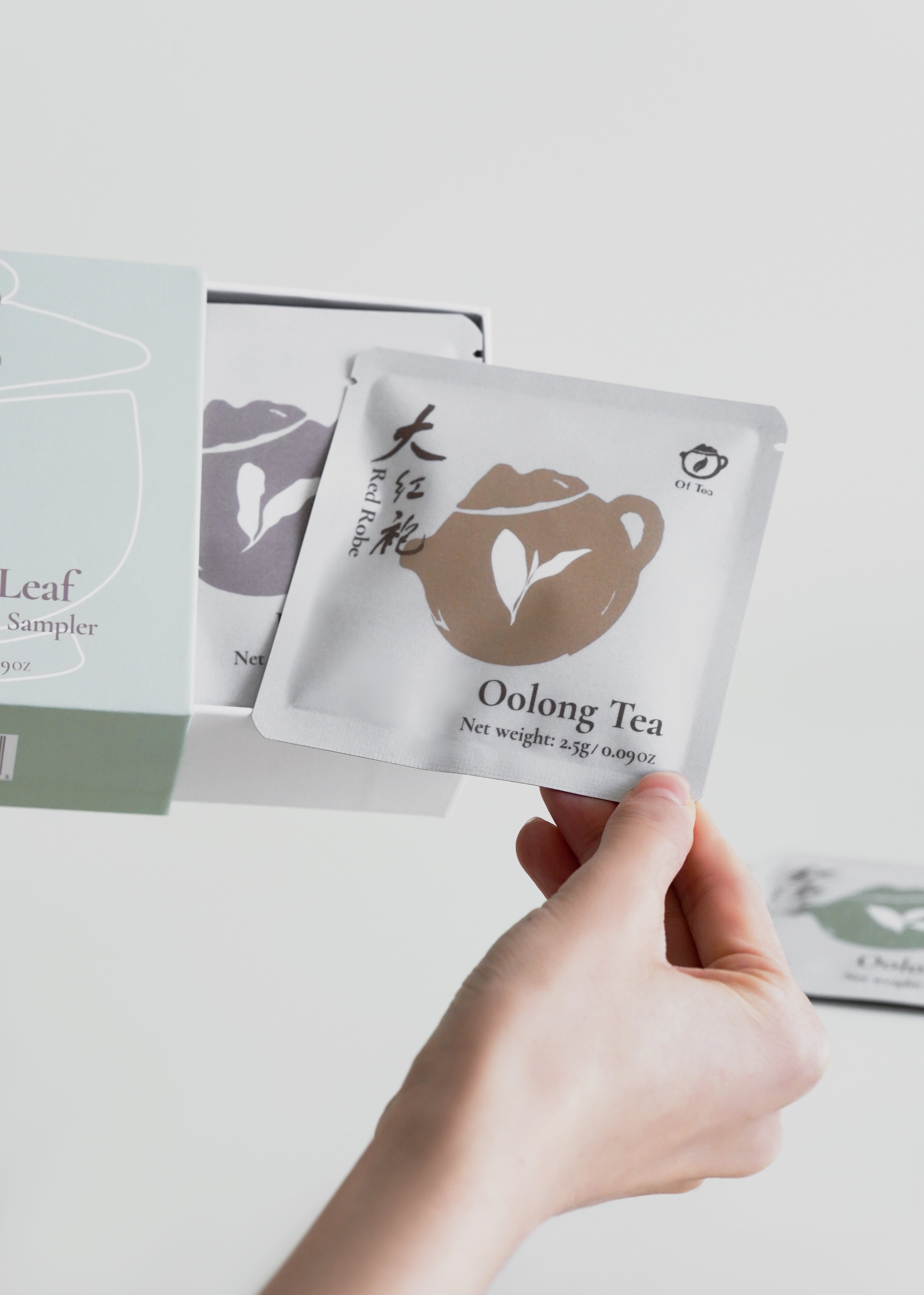 Hand holding a packet of oolong tea with more tea packets in the background on a light surface.