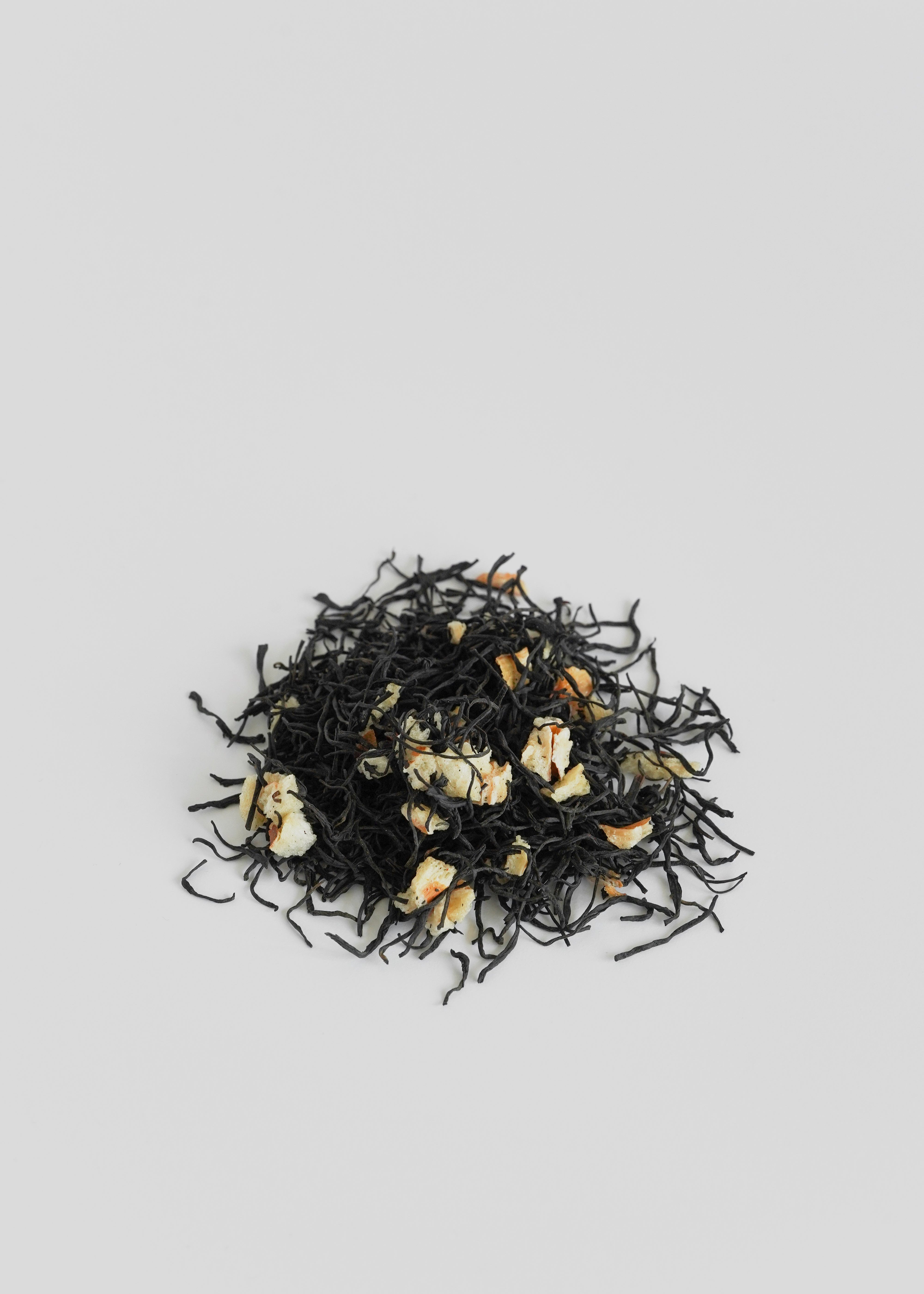 Black tea leaves with gold buds on a light gray background. Lychee black tea