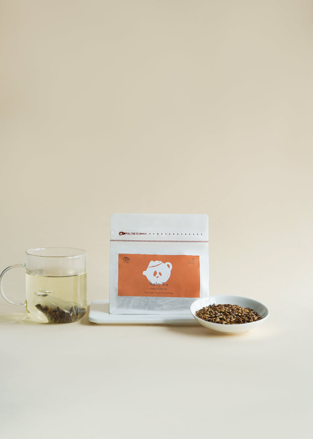 Tea package, glass of tea, and bowl of tea leaves on a beige background