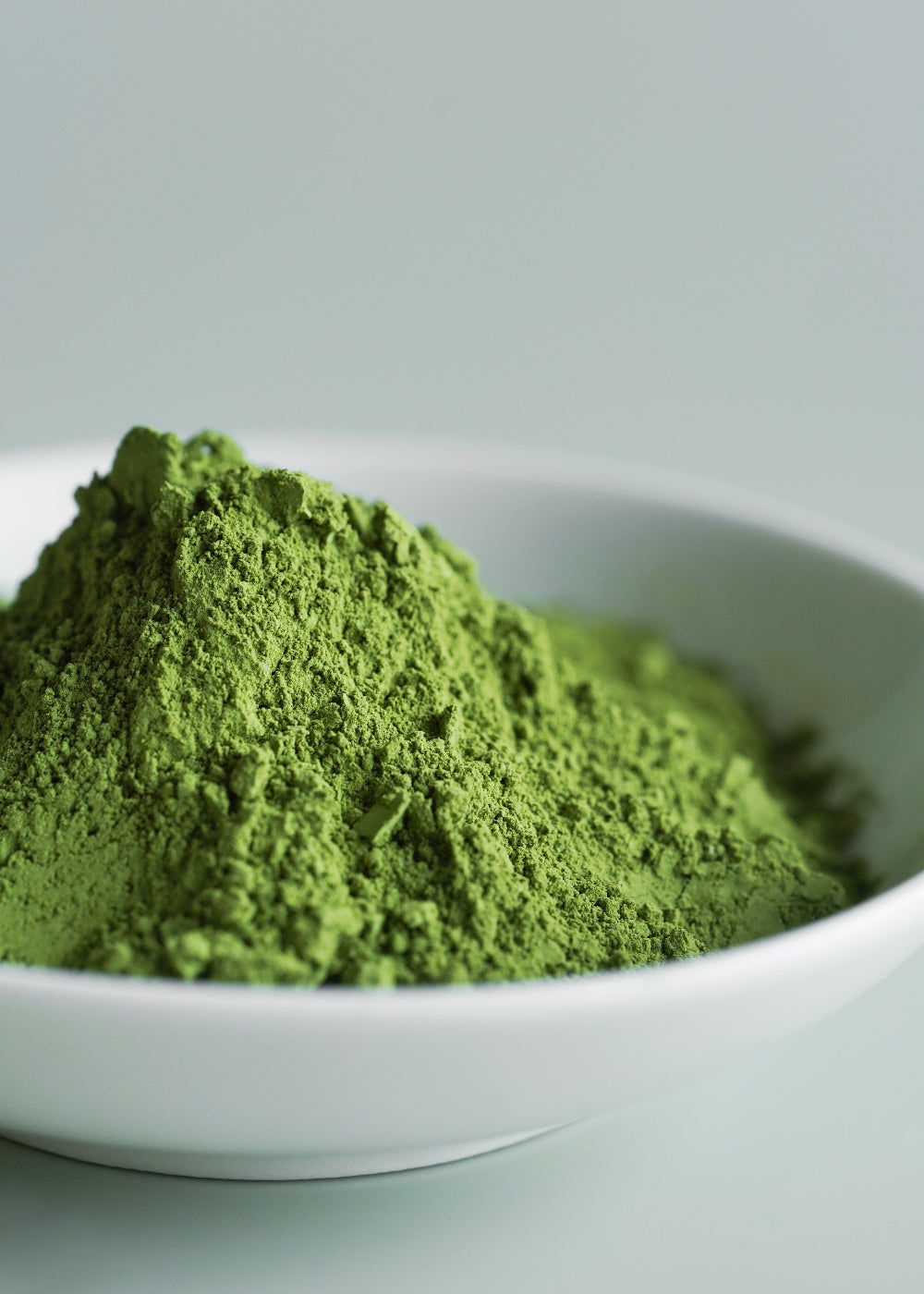 Green powder in a white bowl on a light gray background