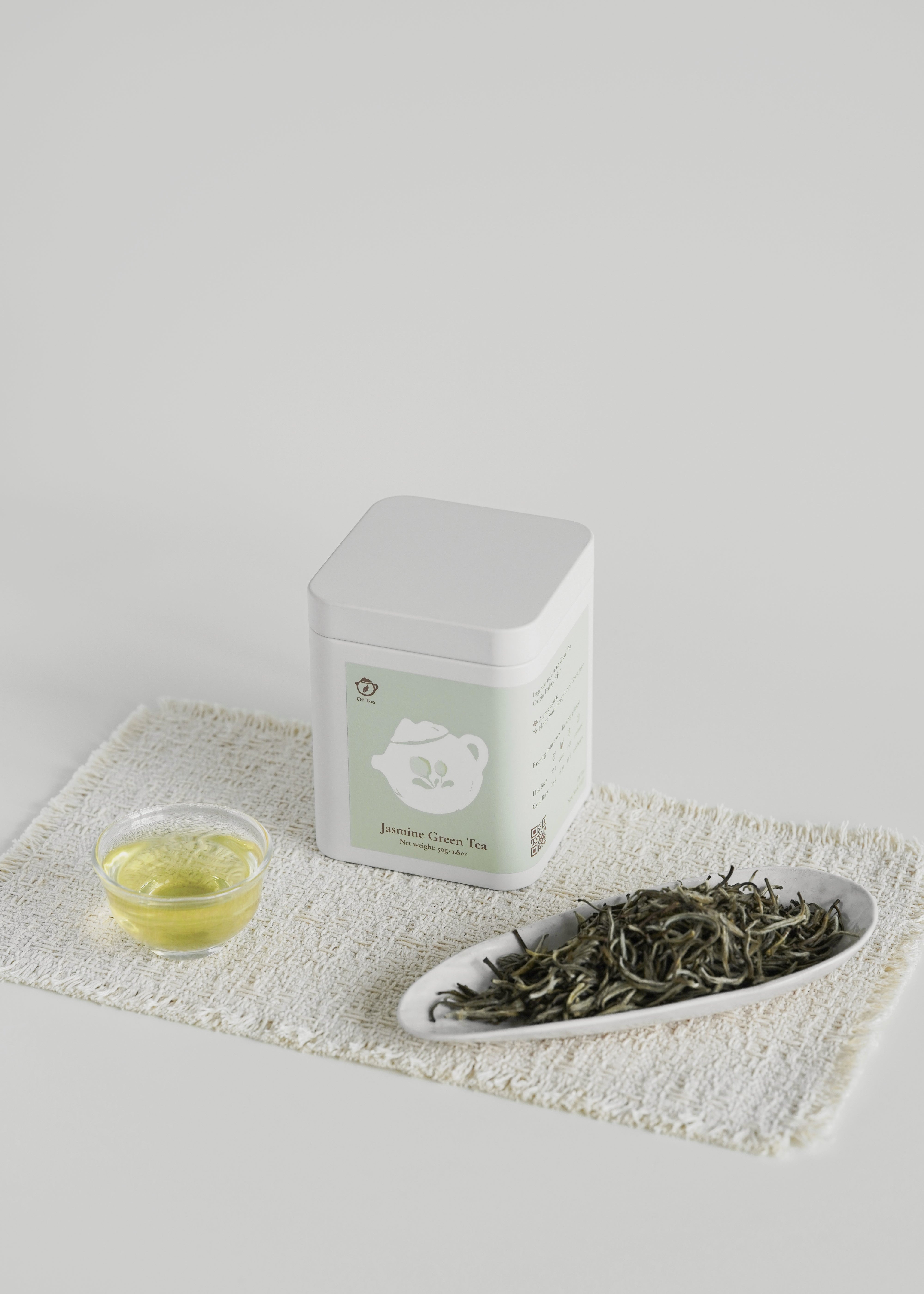 Tea packaging with a small dish of tea leaves and a cup on a white surface. Jasmine green tea