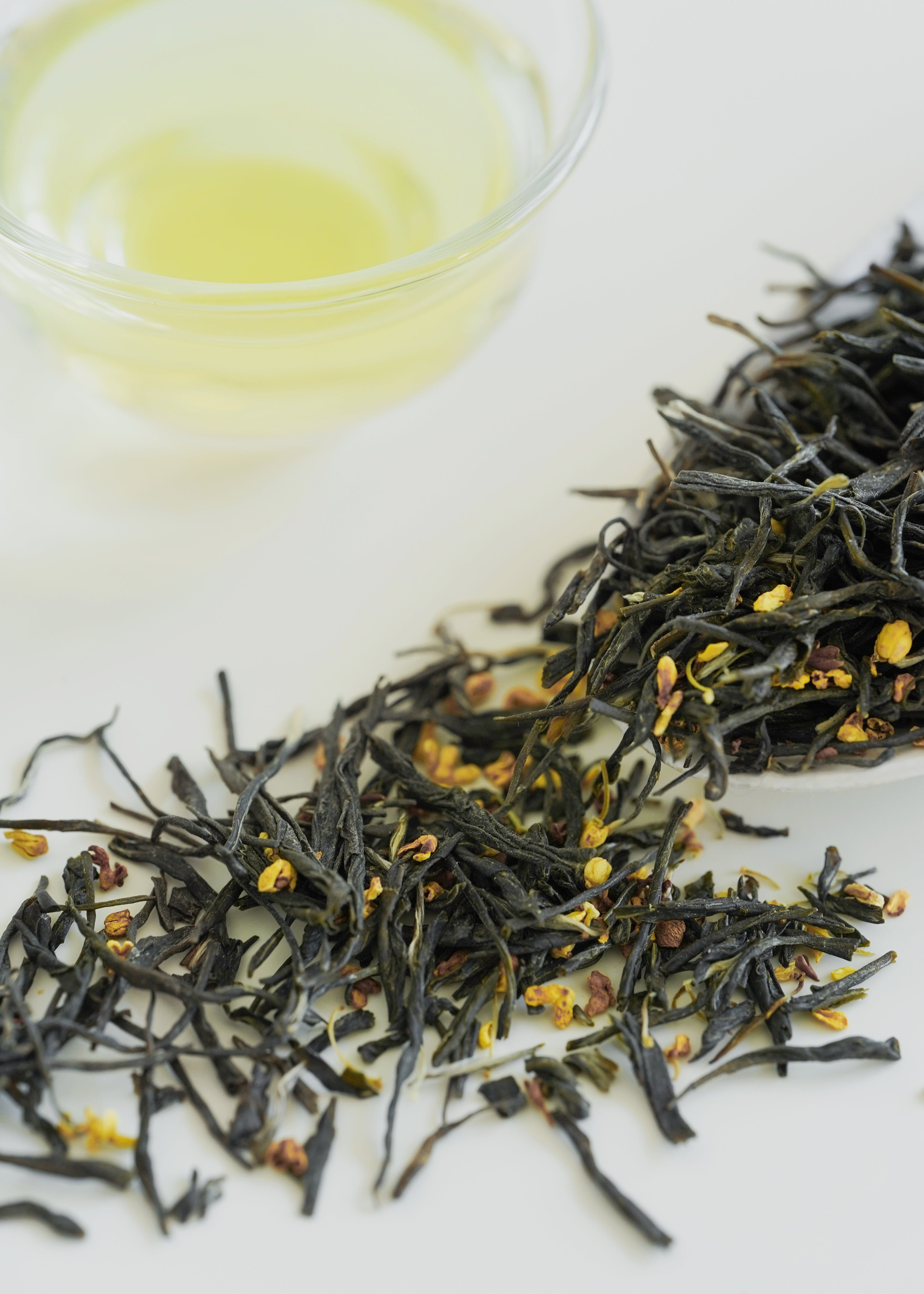 Dry green tea leaves with a small bowl of brewed tea on a white background. Osmanthus Green Tea