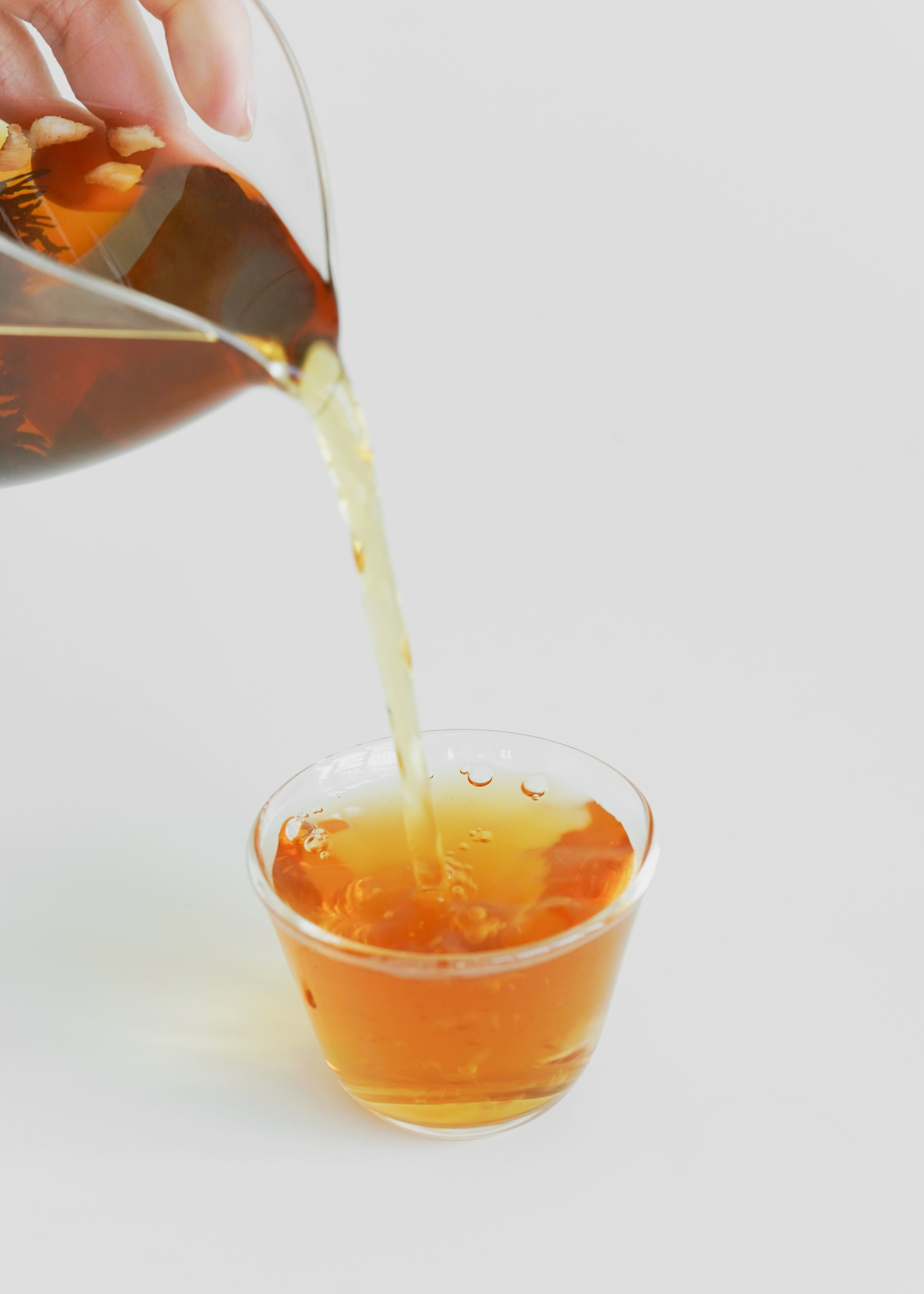 Tea being poured from a pot into a glass cup on a light background. Lychee black tea