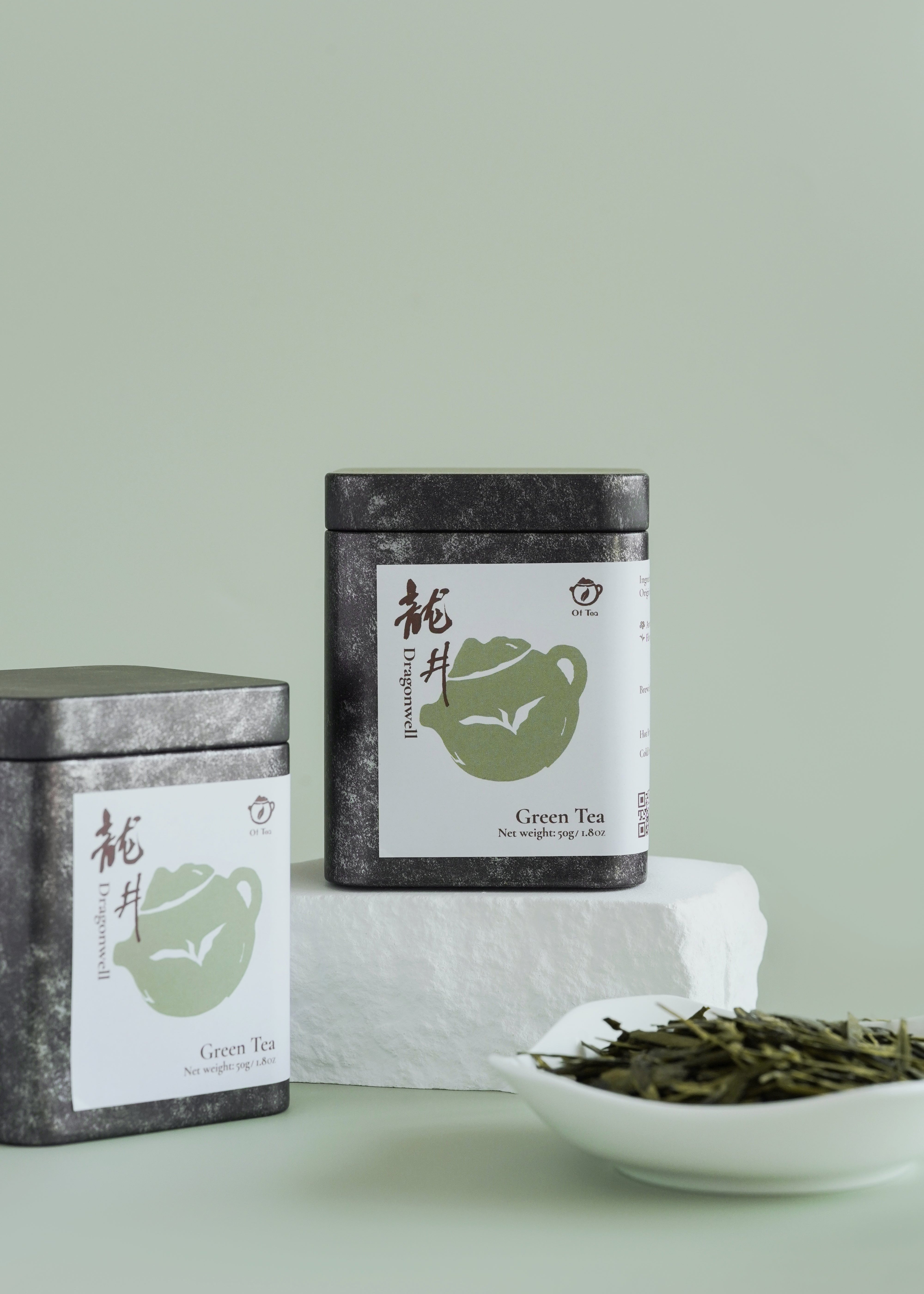 Two tea tins with green tea leaves on a light green background. Dragon well longjing