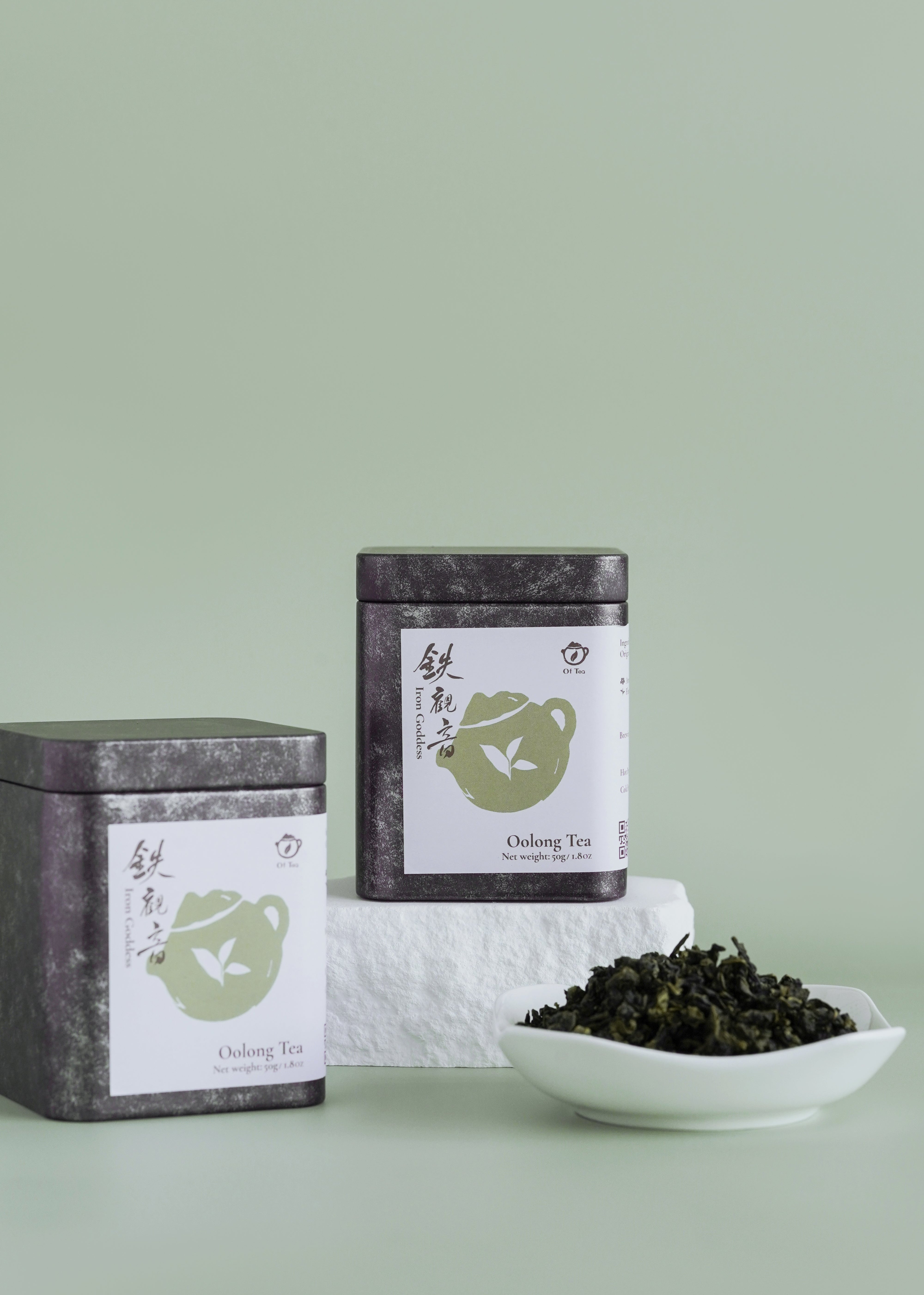 Two tea tins with a bowl of tea leaves on a light green background. Iron Goddess