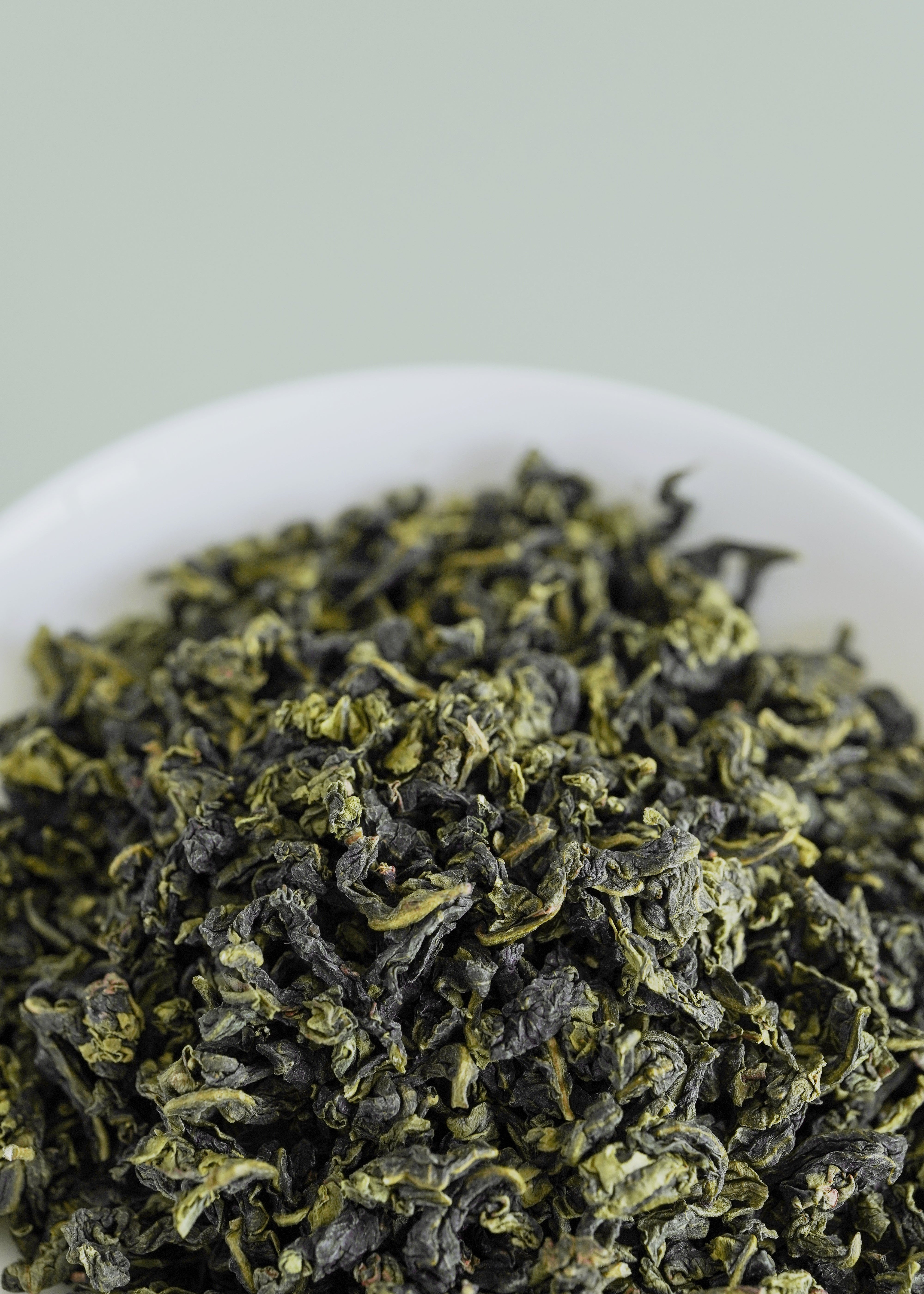 Close-up of green tea leaves on a white plate with a light green background.  Iron Goddess