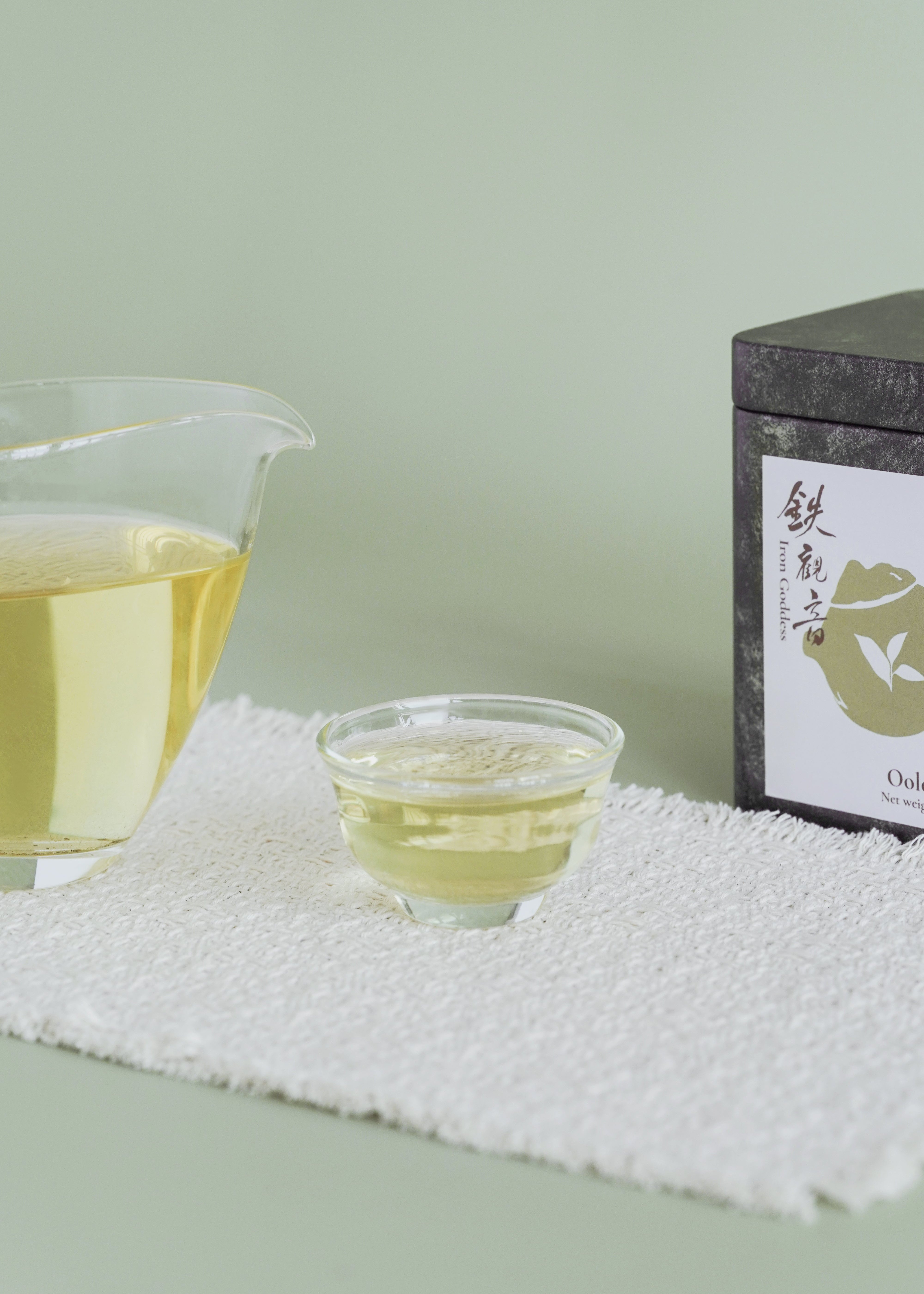 Tea cup and pot with a tea box on a textured surface against a light green background. Iron goddess