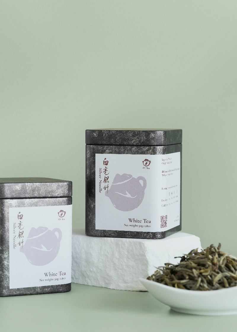 Two tea tins with labels and a bowl of white tea leaves on a light green background. Silver needle 
