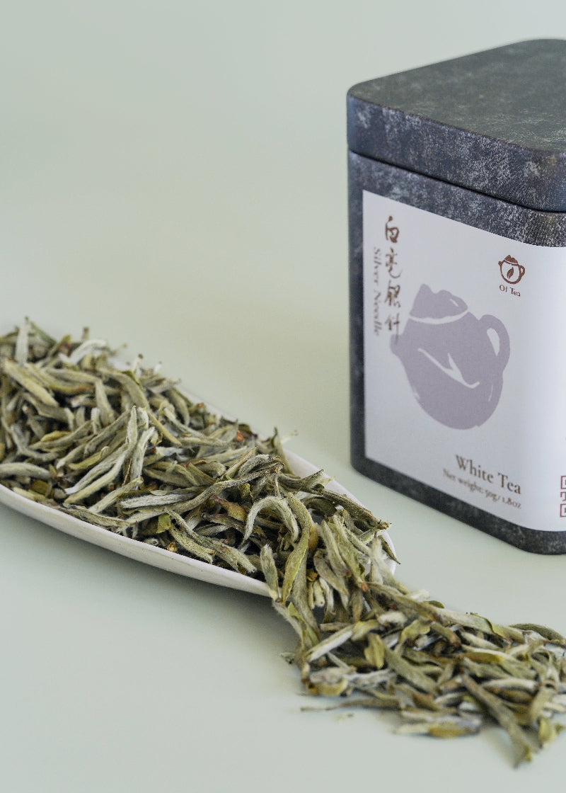 White tea leaves on a white plate with a black tea canister labeled 'White Tea' in the background. SIlver needle