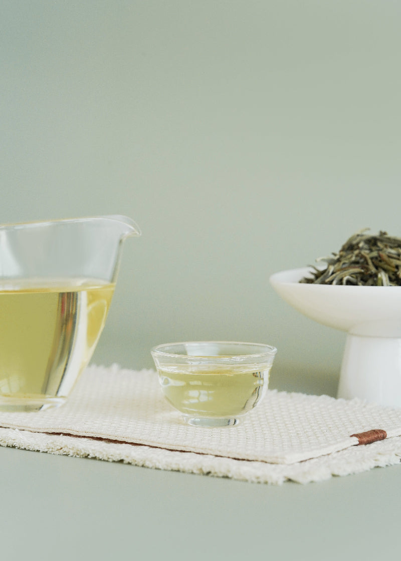 Two cups of green tea on a textured surface with a light green background. SIlver needle