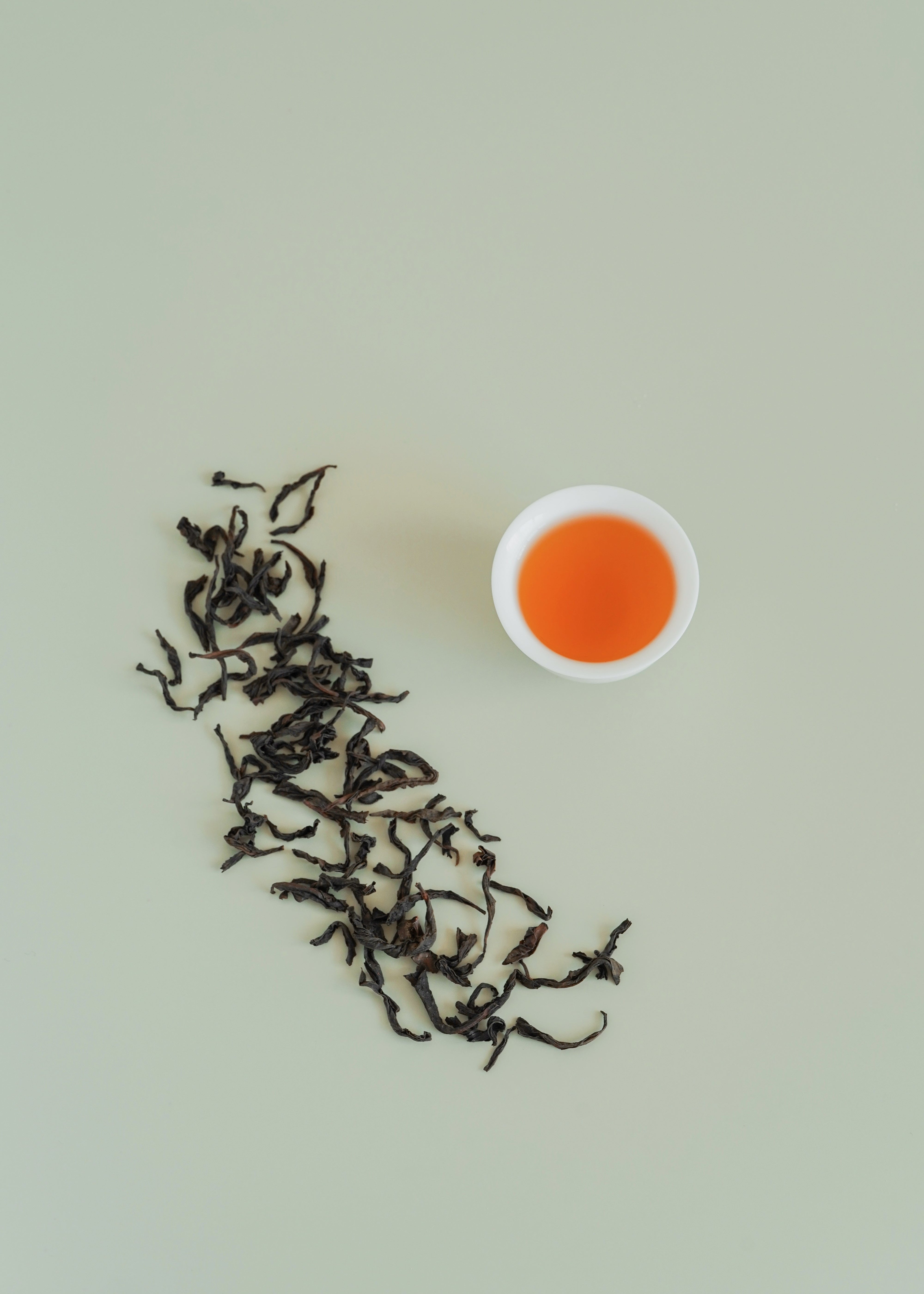 Tea leaves and a cup of tea on a light green background. Big red robe, da hong pao
