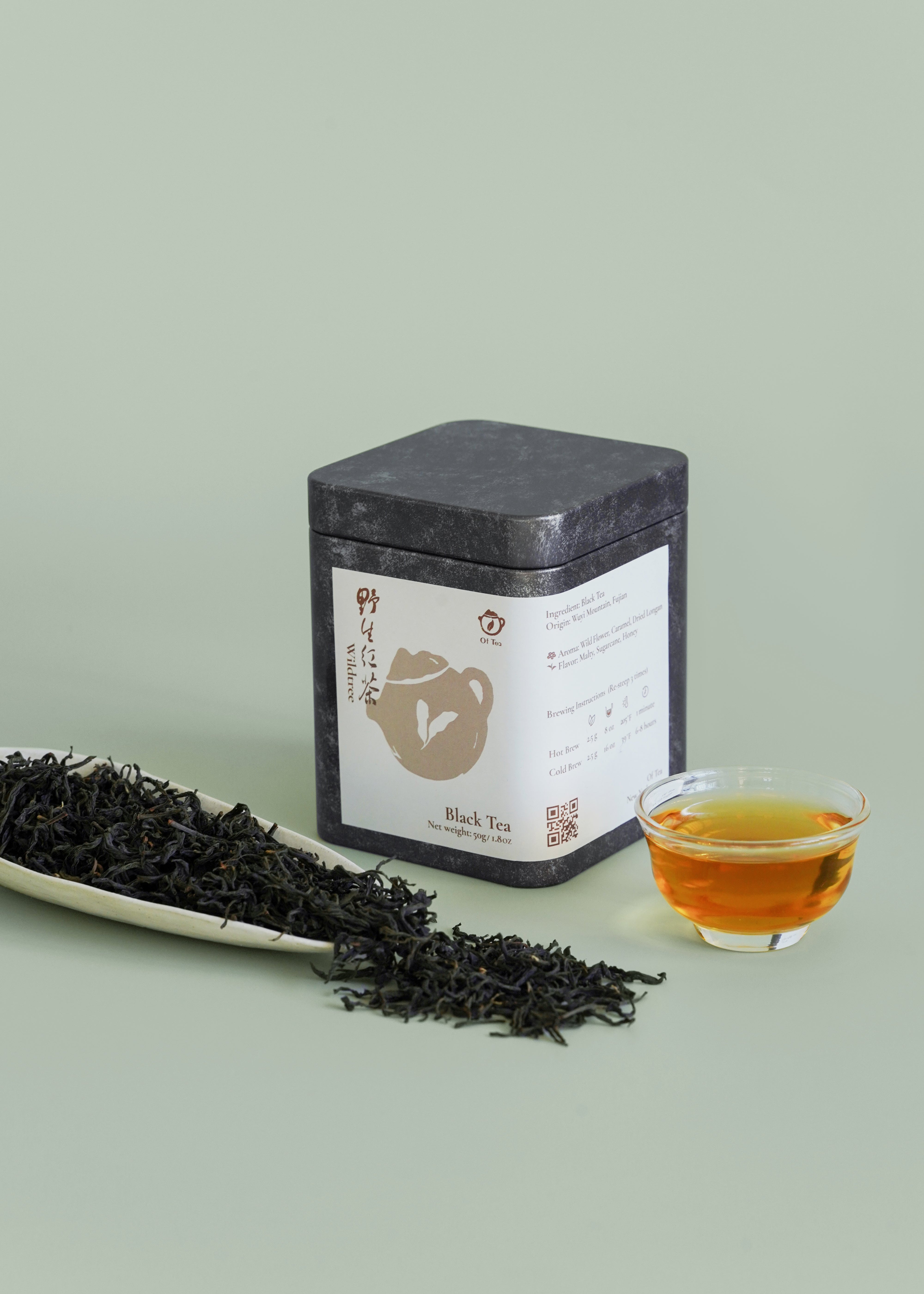 Tea canister with a label, a bowl of tea, and a tray of loose tea leaves on a light green background. Wild tree black tea