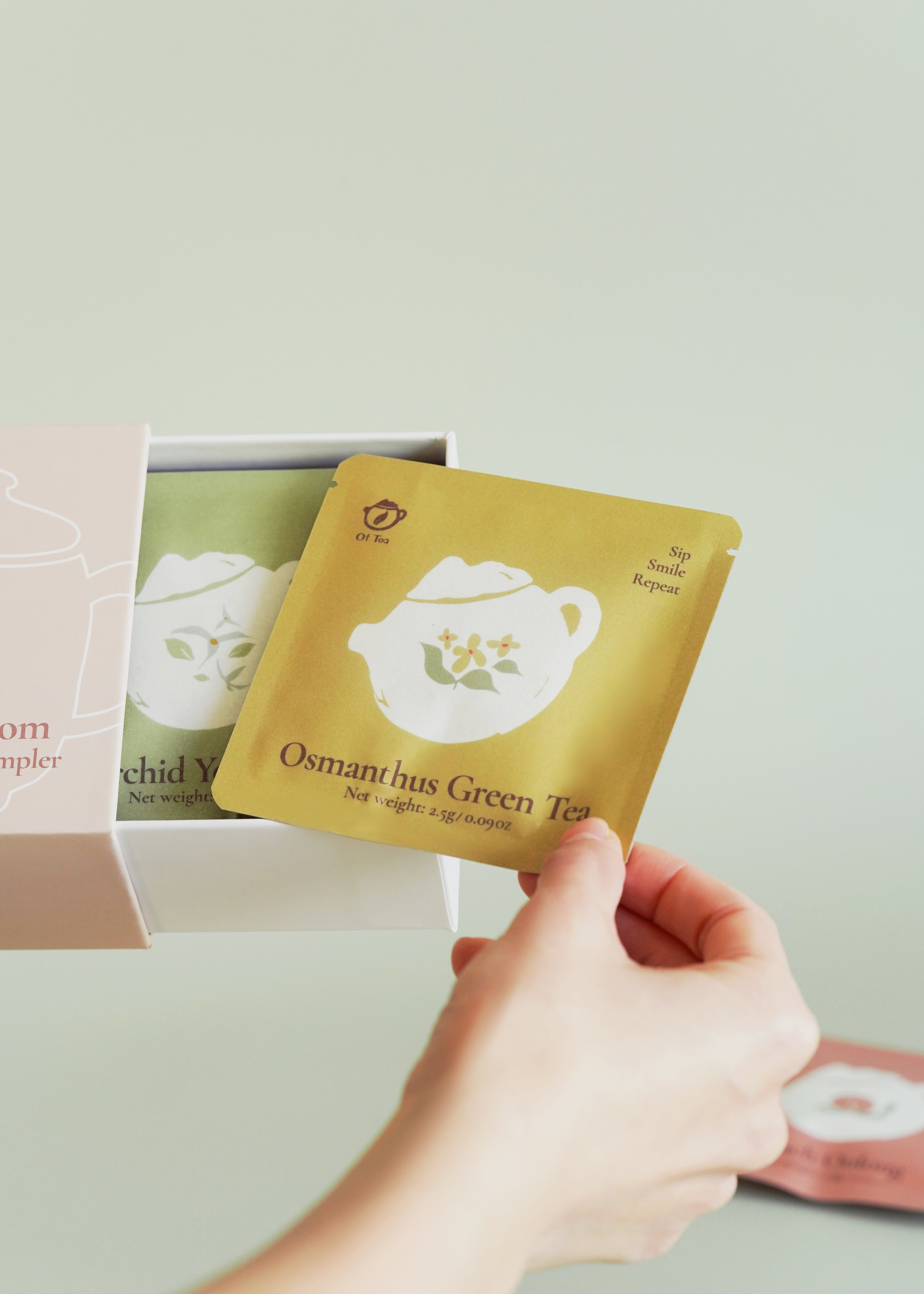 Hand holding a Osmanthus green tea bag with a brand logo against a light background
