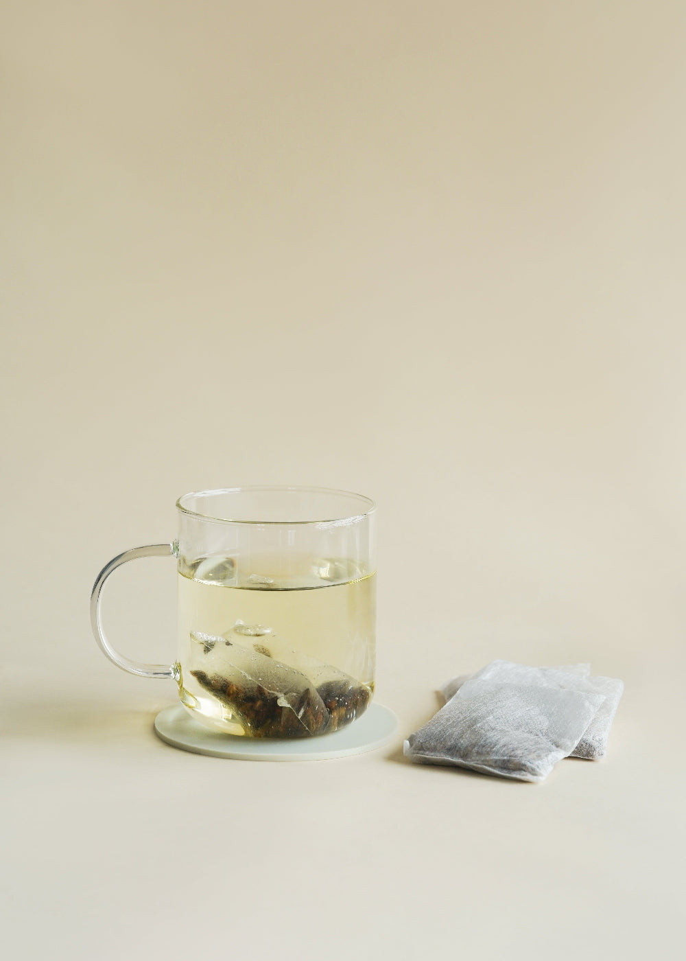 Clear glass mug with green tea and a tea bag on a beige surface