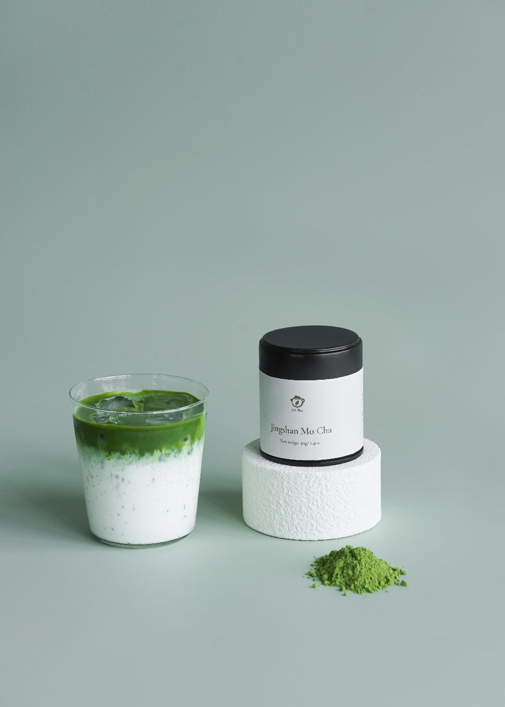 Matcha green tea in a glass with a container of matcha powder on a light gray background